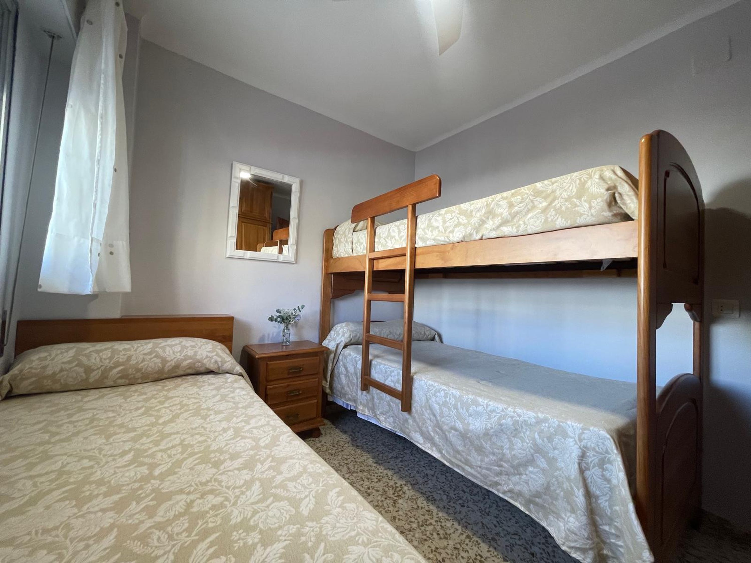 A bedroom with two beds, a nightstand, a mirror, and a window with curtains.