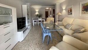 A living room with a glass coffee table, a sofa, a TV, and a dining area with a table and chairs. - Terrasol Estrella 2 in Torre del Mar (Velez-Malaga)