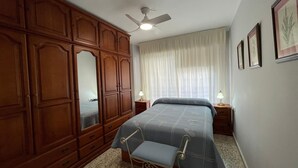 A bedroom with a bed, a wardrobe, a ceiling fan, a window with curtains, bedside lamps, and framed pictures on the wall. - Terrasol Estrella 2 in Torre del Mar (Velez-Malaga)