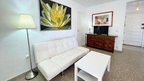 A living room with a white sofa, a white coffee table, a floor lamp, a TV on a wooden cabinet, and a large flower painting on the wall. - Terrasol Trinidad 4 in Torre del Mar (Velez-Malaga)