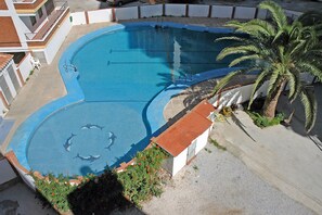Una piscina de forma peculiar, rodeada por un deck de hormigón y una palmera.