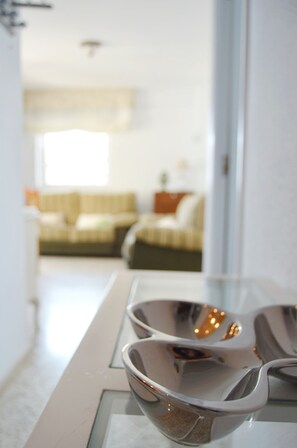 Eine moderne Küche mit Esstisch aus Glas und Blick in ein Wohnzimmer mit Sofa und Fenster.