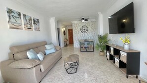 A living room with a sofa, a coffee table, a TV, and a dining area with chairs and a table. - Terrasol Estrella DE MAR (Velez-Malaga)