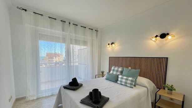 A bedroom with a bed, curtains, a headboard, bedside tables, and a view through the window. - Terrasol Estrella DE MAR (Velez-Malaga)