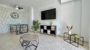 A living room with a TV, a ceiling fan, a dining table, chairs, a potted plant, a side table, and storage units. - Terrasol Estrella DE MAR (Velez-Malaga)