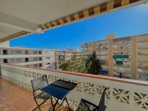 Un balcon avec une table et des chaises, donnant sur un quartier résidentiel composé d’immeubles à plusieurs étages.