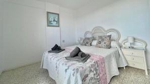 A bedroom with a bed, pillows, a nightstand, a lamp, a ceiling fan, and a framed picture on the wall. - Terrasol Antillas 13 (Velez-Malaga)