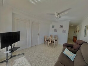 A living room with a TV, a ceiling fan, a dining table with chairs, and a sofa. - Terrasol Antillas 13 (Velez-Malaga)