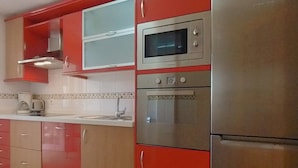 A kitchen with red cabinets, a stainless steel oven, and a microwave. - Terrasol Azucarera 3 Dormitorios (Velez-Malaga)