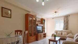 A living room with a television, a sofa, a dining table with chairs, and a cabinet. - Terrasol Azucarera 3 Dormitorios (Velez-Malaga)
