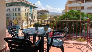 A balcony with a table and chairs, overlooking a cityscape with buildings and a mountain in the distance. - Terrasol Azucarera 3 Dormitorios (Velez-Malaga)