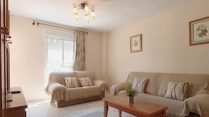 A living room with two sofas, a coffee table, a chandelier, and a window with curtains. - Terrasol Azucarera 3 Dormitorios (Velez-Malaga)