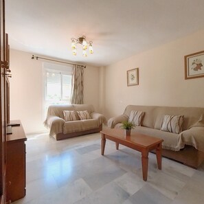A living room with two sofas, a coffee table, a chandelier, and a window with curtains. - Terrasol Azucarera 3 Dormitorios (Velez-Malaga)