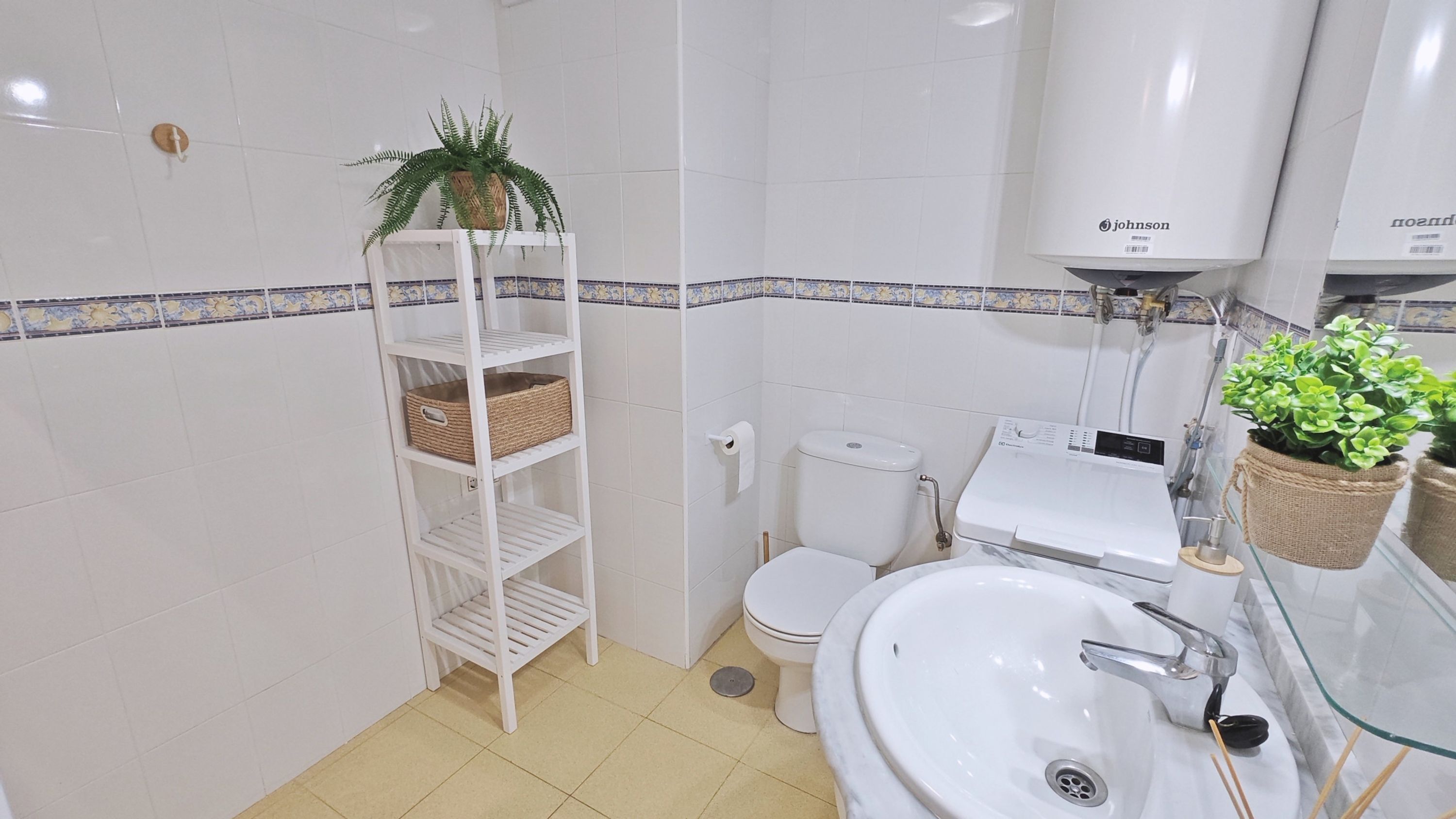 Een badkamer met een witte wastafel, toilet en plank met manden.