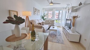 A modern living room with a glass dining table, a sofa, a TV, and a ceiling fan. - Terrasol Franlou Vistas AL MAR (Velez-Malaga)