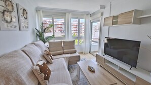 A modern living room with a sofa, TV, and a large window with a view of buildings. - Terrasol Franlou Vistas AL MAR (Velez-Malaga)