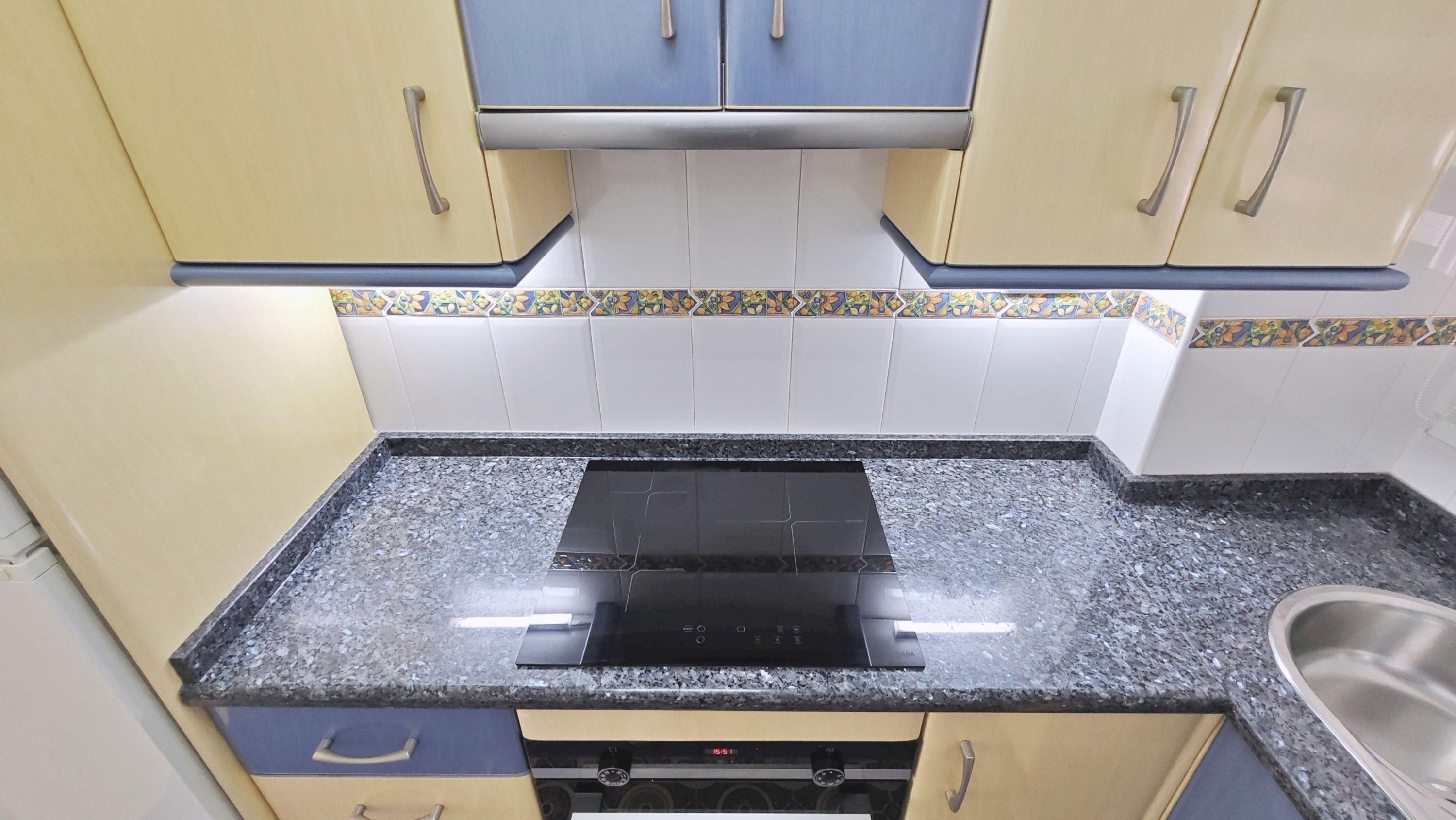A compact kitchen with a black stove, white tiled backsplash, and light-colored cabinets.