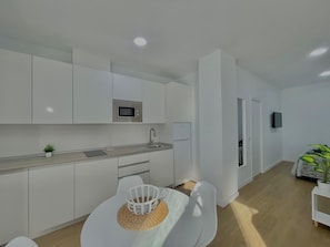 Een moderne keuken met witte kastjes, een magnetron en een spoelbak. Er is een eethoek met een witte tafel en stoelen.
