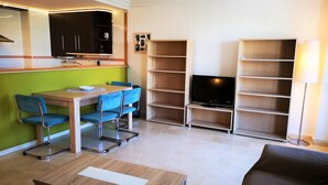 Espai vital compacte amb zona de dinar, sofà, televisió sobre un suport i una làmpada.