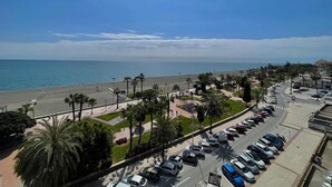 Una strada costiera con auto parcheggiate, una spiaggia e palme.