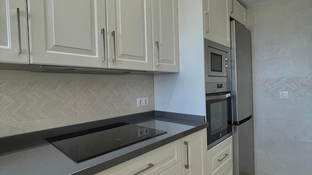 Una cucina con mobili bianchi, un piano di lavoro nero, un forno a microonde integrato, un forno e una lavastoviglie.