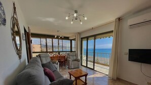 Un soggiorno con divano, poltrone, tavolo, televisore e un balcone con vista sul mare.