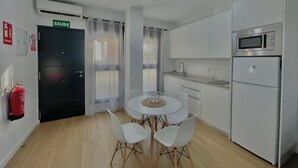 A modern kitchen with white cabinets, a microwave, and a refrigerator. There is a dining table with chairs and a fire extinguisher on the wall. - Terrasol Maenoba Playa 3 (Velez-Malaga)