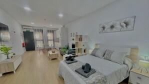 A modern hotel room with a large bed, a desk, a chair, a small table, and a bookshelf. - Terrasol Maenoba Playa 3 (Velez-Malaga)