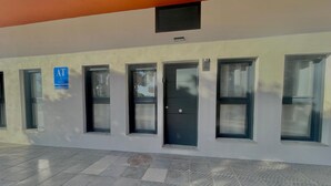 A building facade with multiple windows and doors, a blue sign indicating a location, and a tiled floor. - Terrasol Maenoba Playa 3 (Velez-Malaga)