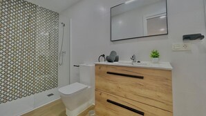 A modern bathroom with a toilet, shower, and vanity with a mirror. - Terrasol Maenoba Playa 3 (Velez-Malaga)