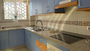 A kitchen with blue cabinets, a stainless steel sink, a built-in stove, and a window with a decorative curtain. - Terrasol Roma 9 in Torre del Mar (Velez-Malaga)