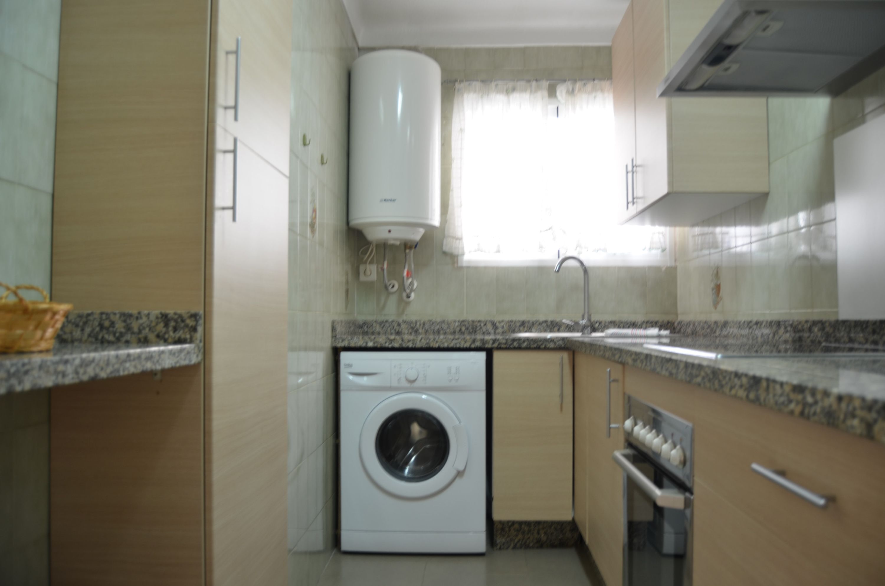A compact kitchen with a built-in washer, a sink, and a window with curtains.