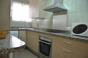 A kitchen with granite countertops, a built-in oven, a microwave, and a window with curtains. - Terrasol Puerto Blanco 3-b1 Frontal AL MAR (Velez-Malaga)
