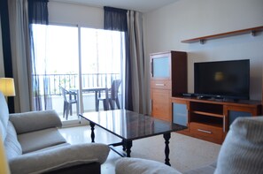 Ein Hotelzimmer mit einer Sitzecke, einem Glastisch, einem Fernseher auf einem Holzboden, einem Schrank und einem Balkon mit Blick.
