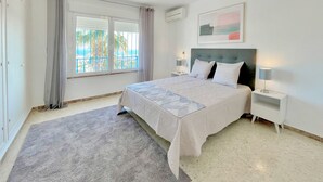 A bedroom with a bed, two bedside tables, a window with curtains, an air conditioning unit, and a painting on the wall. - Terrasol Villa Independiente Y Apartamento (Velez-Malaga)