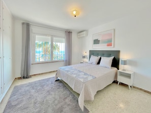 A bedroom with a bed, two bedside tables, a window with curtains, an air conditioning unit, and a painting on the wall. - Terrasol Villa Independiente Y Apartamento (Velez-Malaga)