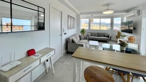 A modern apartment with a dining area, sofa, TV, and a view of the city. - Terrasol Plazamar 2-9-14 (Velez-Malaga)