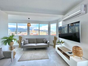Ein modernes Wohnzimmer mit einer Couch, einem Fernseher, einem Kaktus und Blick auf die Stadt.