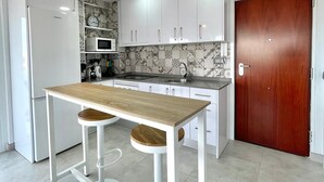 A modern kitchen with white cabinets, a wooden table, two bar stools, a hanging light fixture, and a microwave. - Terrasol Plazamar 2-9-14 (Velez-Malaga)