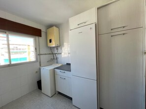 Eine kompakte Küche mit Waschmaschine, Kühlschrank und Fenster mit Blick auf Gebäude.