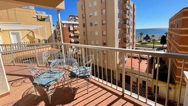 A balcony with a table and chairs, overlooking a coastal area with buildings and a clear sky. - Terrasol Rismar 4 in Torre del Mar (Velez-Malaga)