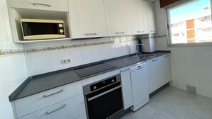 A kitchen with white cabinets, a microwave, a dishwasher, and a window with a view of buildings. - Terrasol Rismar 4 in Torre del Mar (Velez-Malaga)
