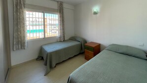 A room with two single beds, a small wooden dresser, a window with curtains, and a wall-mounted light fixture. - Terrasol Rismar 4 in Torre del Mar (Velez-Malaga)