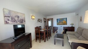A living room with a TV, wooden dining table, chairs, a sofa, and artwork on the walls. - Terrasol Rismar 4 in Torre del Mar (Velez-Malaga)