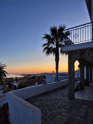 A stone-paved terrace with a palm tree, a balcony with wrought iron railings, and a view of the sea at sunset. - Terrasol Villa Independiente Caleta DE SOL (Velez-Malaga)