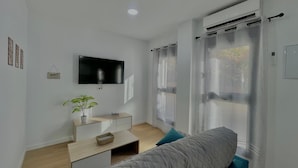A modern room with a bed, a TV, a desk, and a plant. - Terrasol Maenoba Playa 2 (Velez-Malaga)