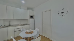 A compact kitchen with white cabinets, a microwave, and a sink. There is a dining table with four white chairs and a clock on the wall. - Terrasol Maenoba Playa 2 (Velez-Malaga)