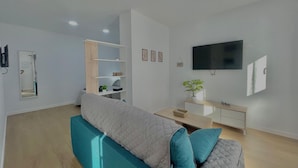 A modern living room with a sofa, a TV, a bookshelf, and a mirror. - Terrasol Maenoba Playa 2 (Velez-Malaga)