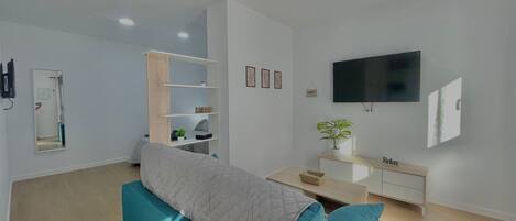A modern living room with a sofa, a TV, a bookshelf, and a mirror.
