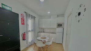 A compact kitchen with white cabinets, a microwave, and a dining table with chairs. There's a fire extinguisher on the wall and a 'SALIDA' sign above a door. - Terrasol Maenoba Playa 2 (Velez-Malaga)